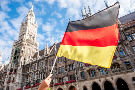 Die Hand hält die Deutsche Flagge, das Rathaus ist im Hintergrund